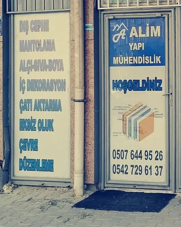Alim Yapı dükkânının eski kırmızı tabelalı cephesi ve kapıdaki hizmet listesi panosu, önde kiremit ve yalıtım malzemeleri