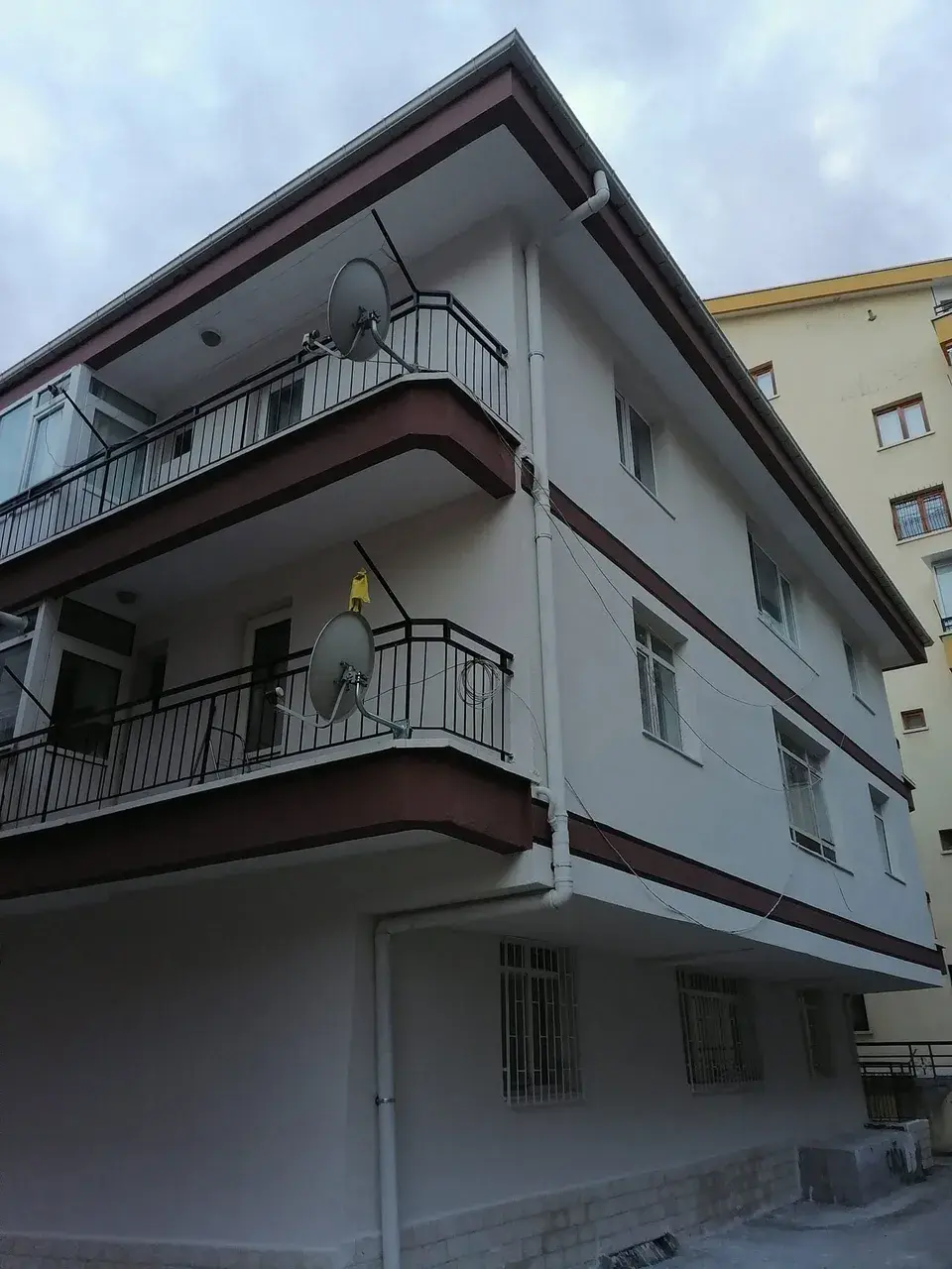 Krem cepheli apartmanın köşeden alttan görünümü, kahverengi balkon alınları ve şeritler